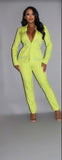 Bright lime green powersuit with rhinestone lettering on blazer, featuring plunging neckline and slim-fit pants, worn by model against gray background