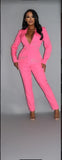 Vibrant pink powersuit with rhinestone letterings on blazer, featuring fitted pants and plunging neckline, modeled against grey background, showcasing glamorous and confident style