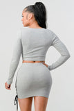 Back view of grey two-piece set featuring cropped long sleeve top and mini skirt with side lace-up detail, worn by model with long dark ponytail